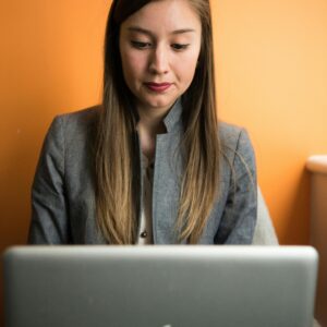 Focused businesswoman using a laptop indoors with an orange background.