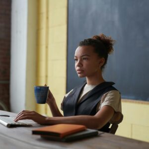 A professional young woman concentrating on work at a desk with a computer and coffee cup in hand.