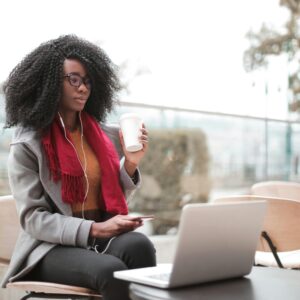 Confident woman working remotely in an outdoor café, sipping coffee and using a laptop.